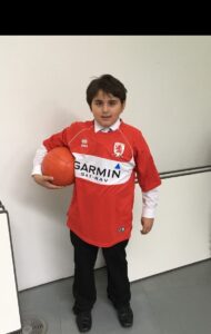 A pupil in Middlesbrough shirt holds a ball under his arm