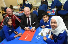 Foundation staff member smiling with local MP and three school pupils as they take part in some arts and crafts.